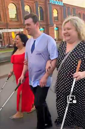 Trzy osoby z białymi laskami idą razem przez rynek Manufaktury w Łodzi, trzymając się na wysokości zgiętego łokcia. To założyciele Fundacji ROWON – Horyzont Możliwości.